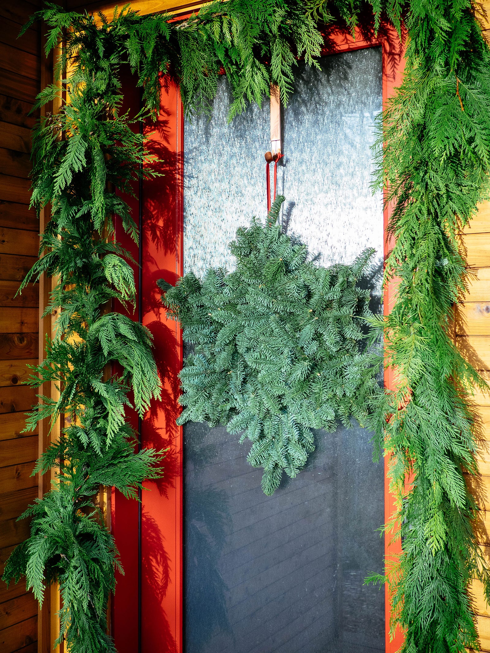 A glass-paneled front door adorned with a snowflake-shaped wreath and cedar garland