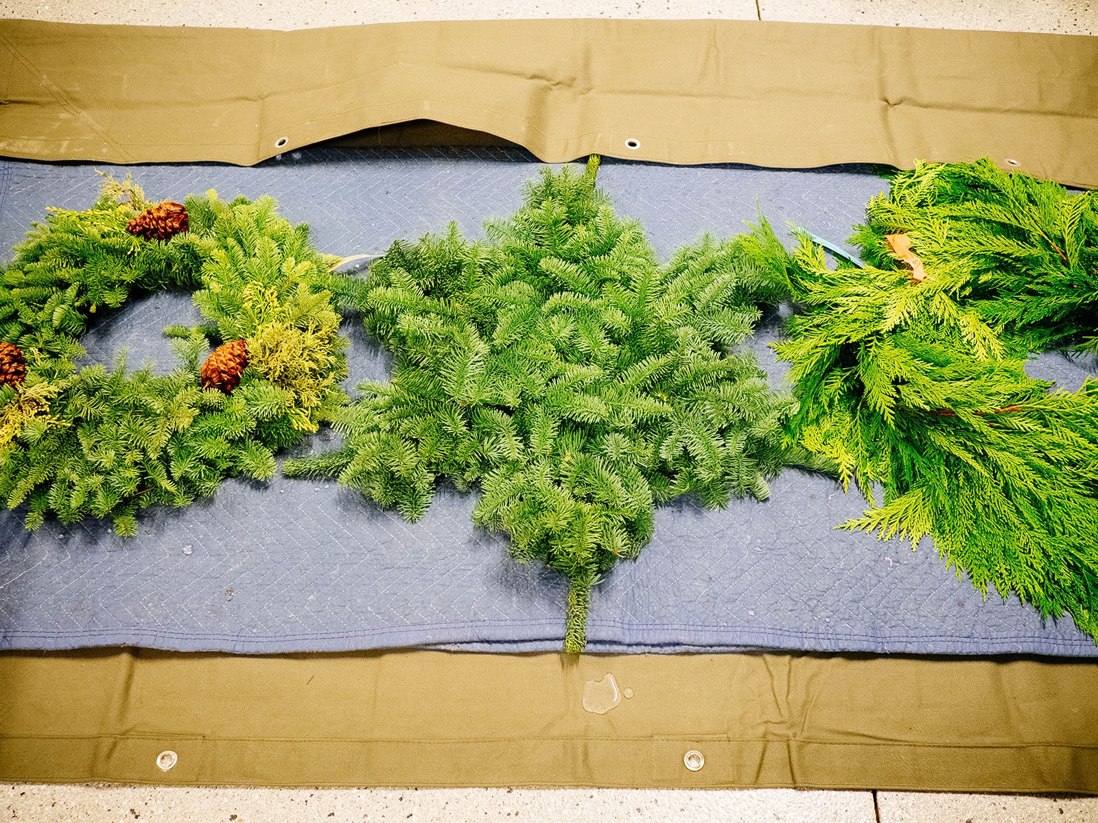 Two wreaths and a garland drip drying on a moving blanket after being soaked in water overnight