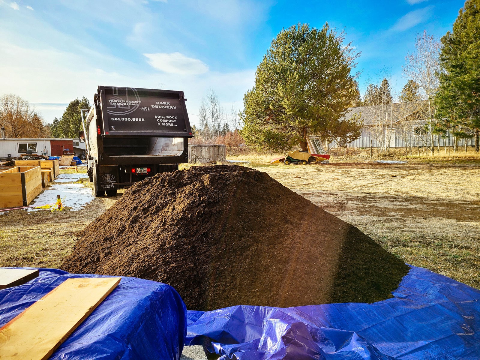 A landscaping truck dumping a load of soil in a yard