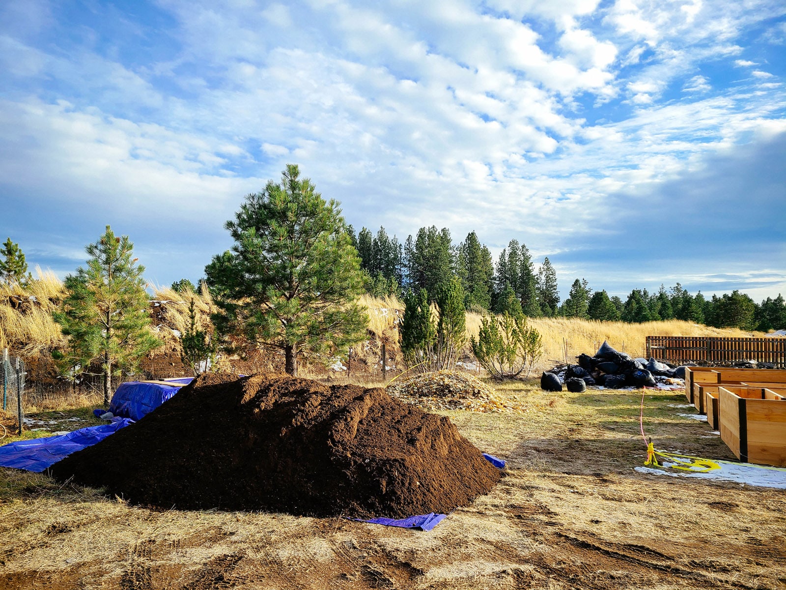 A large mound of topsoil piled on a blue tarp in a garden