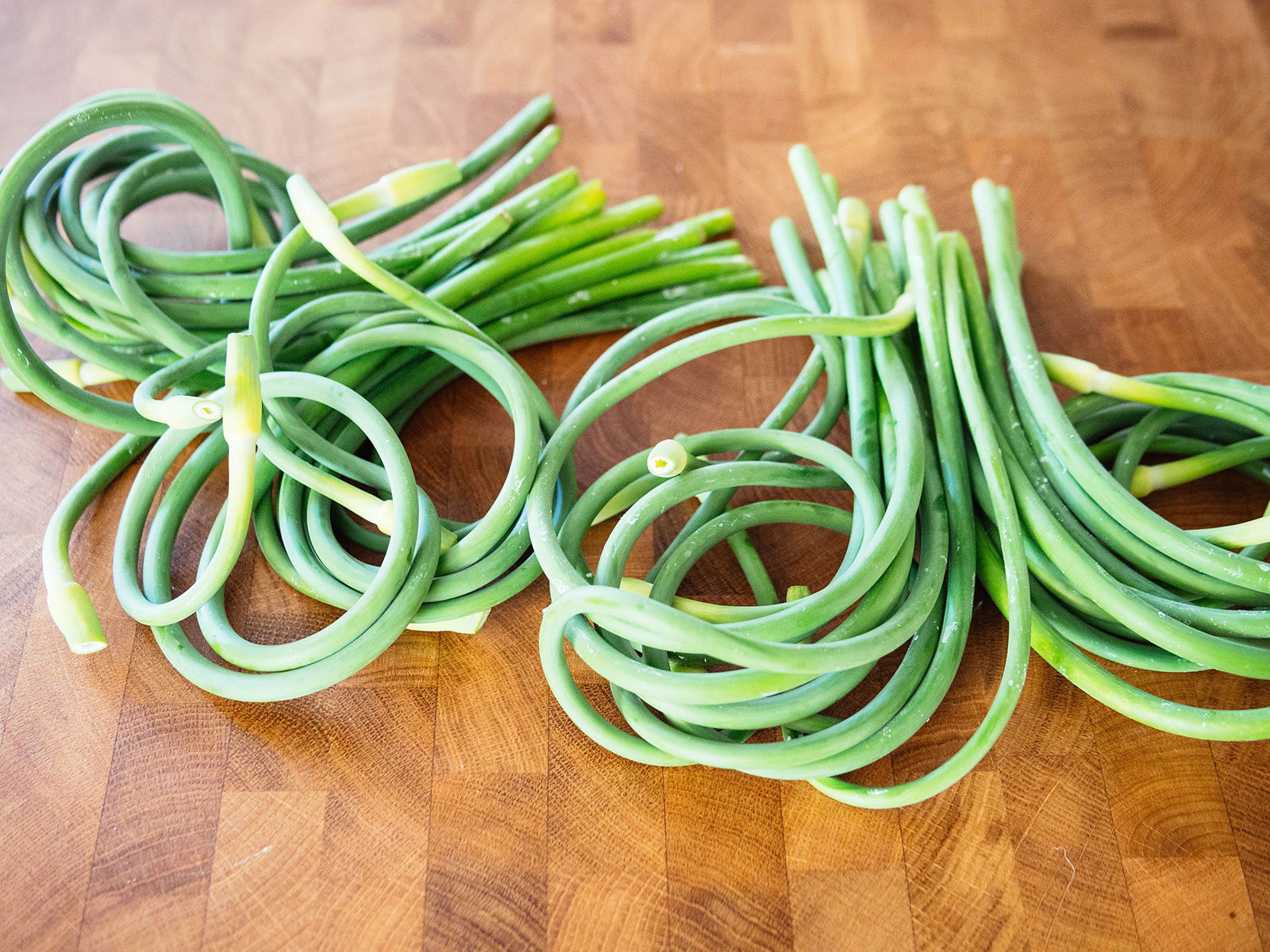 Two bundles of garlic scapes on a butcher block counter