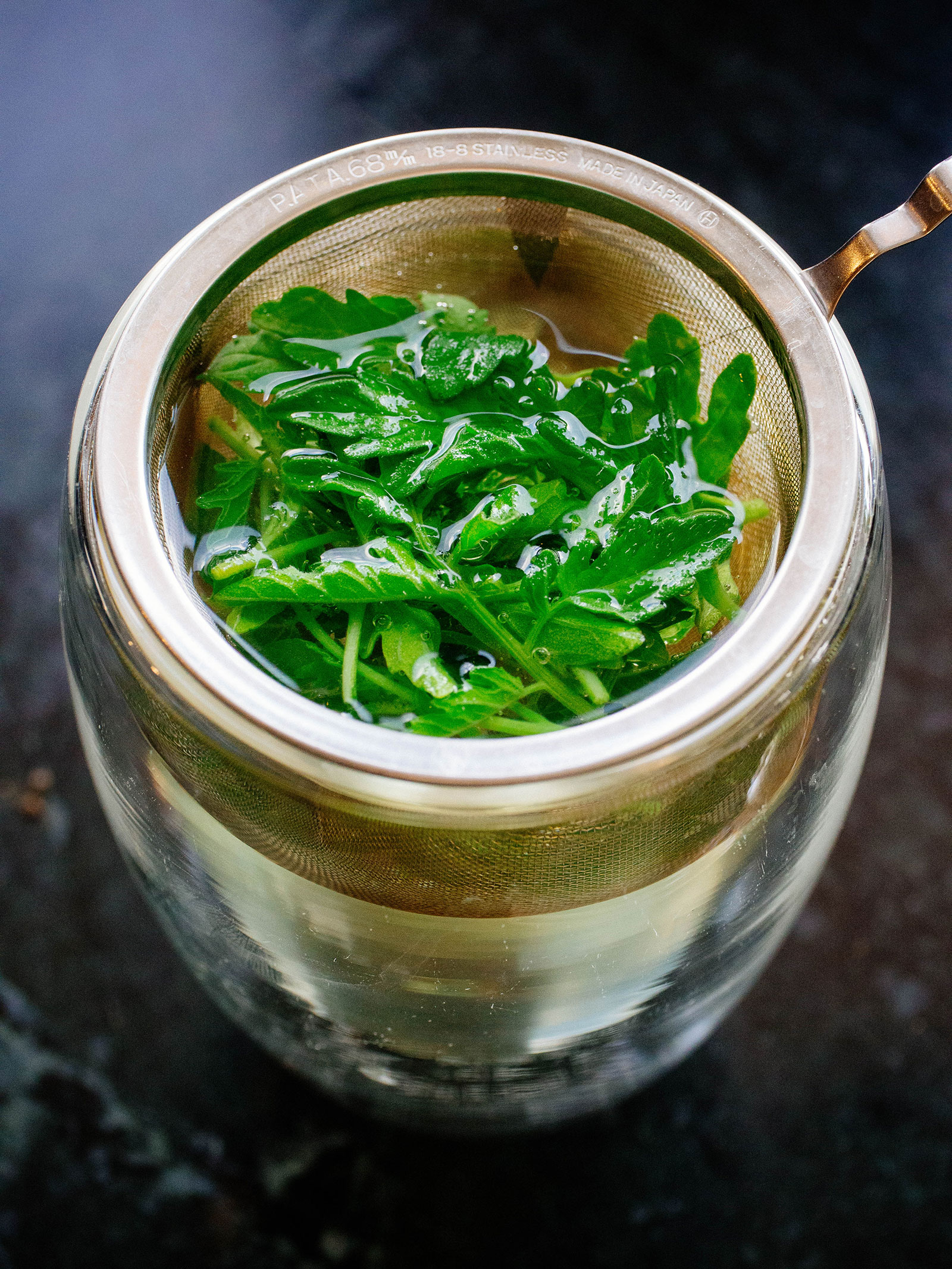 Glass cup holding a metal strainer of tomato leaves steeping in hot water