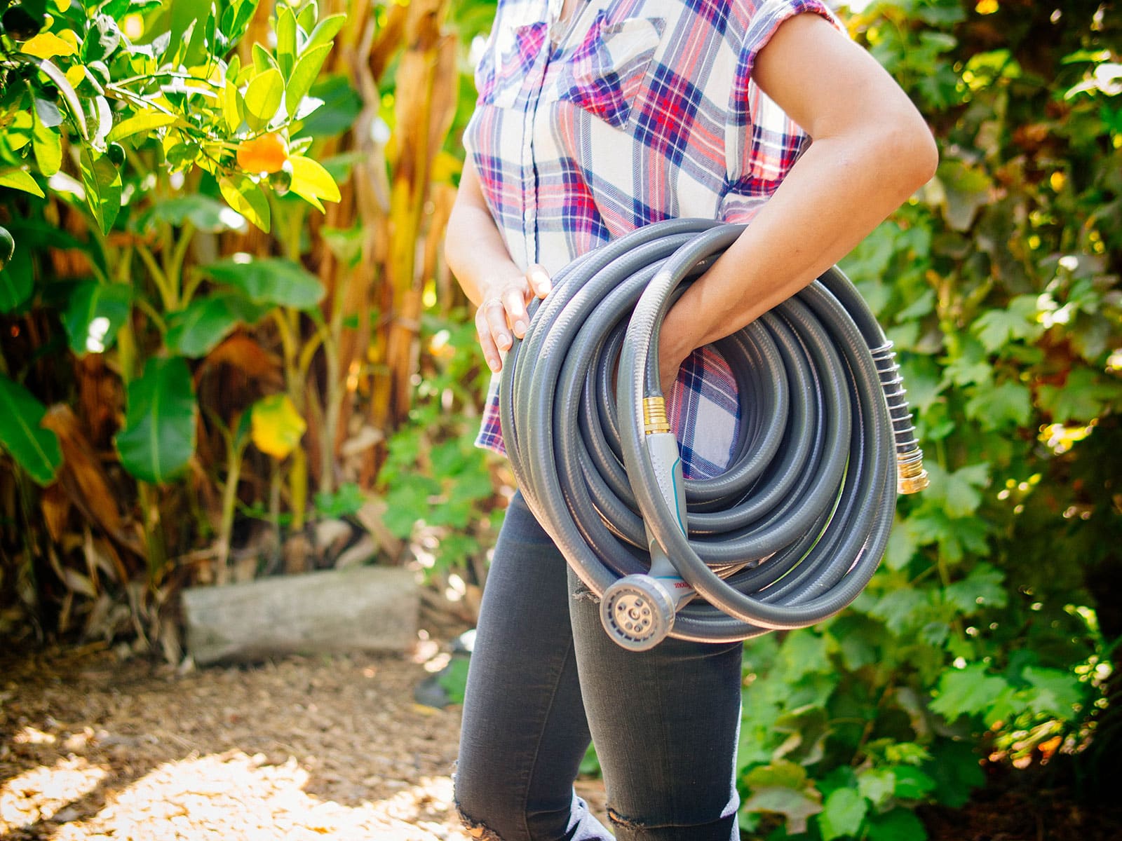 Woman in a plaid shirt and jeans carrying a coil of gray garden hose