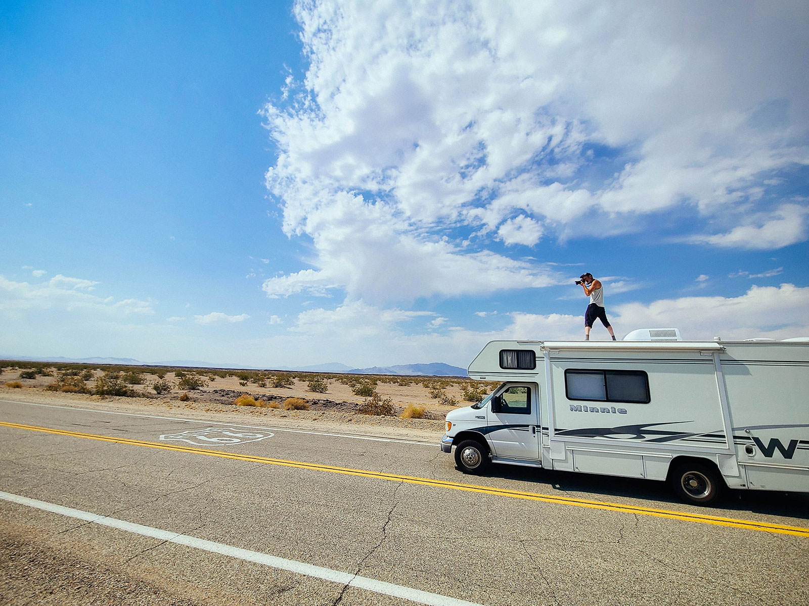 Man standing on the roof of an RV to photograph a Route 66 road emblem