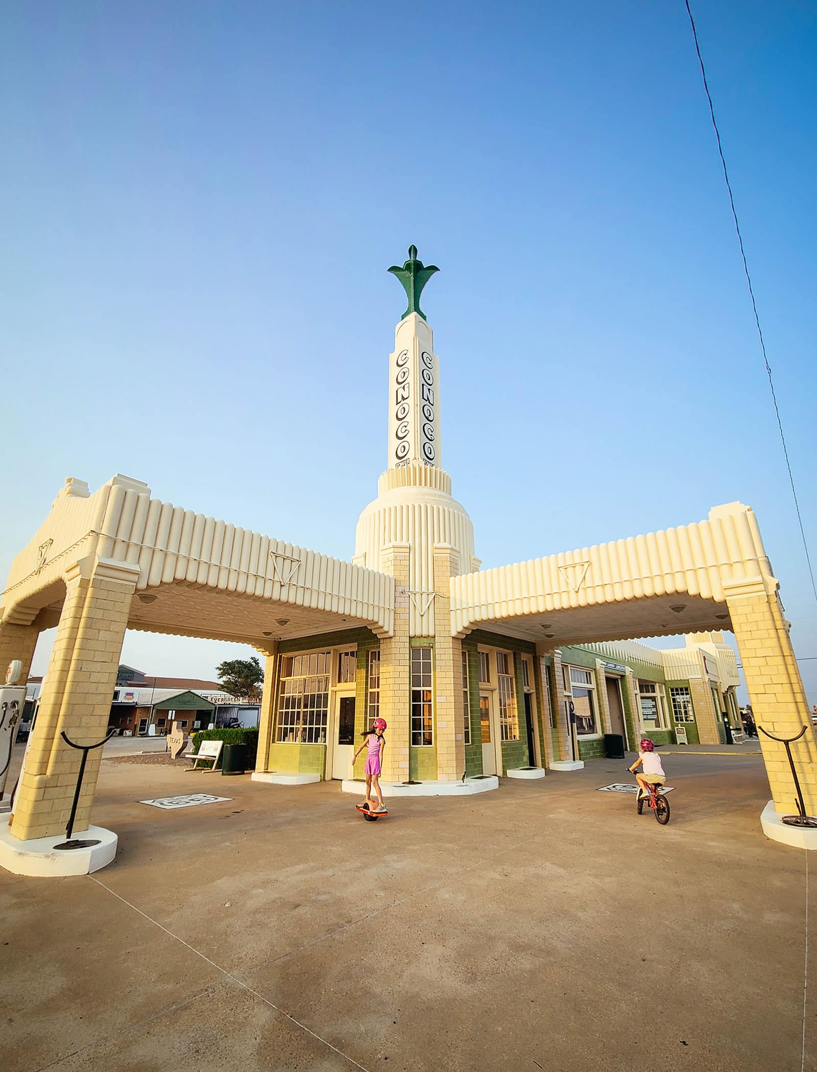 Two young kids biking in front of the restored vintage Conoco filling station on Route 66 in Shamrock, Texas