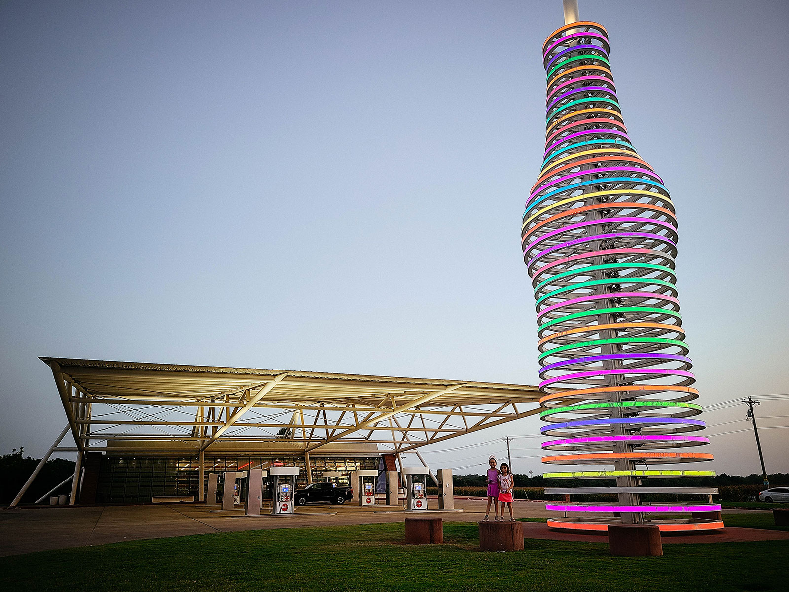 Two kids standing next to the iconic LED-lit soda bottle sculpture at Pops 66 in Arcadia, Oklahoma