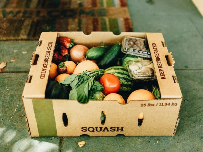 Cardboard CSA box on a green porch, filled with locally grown vegetables and fruits
