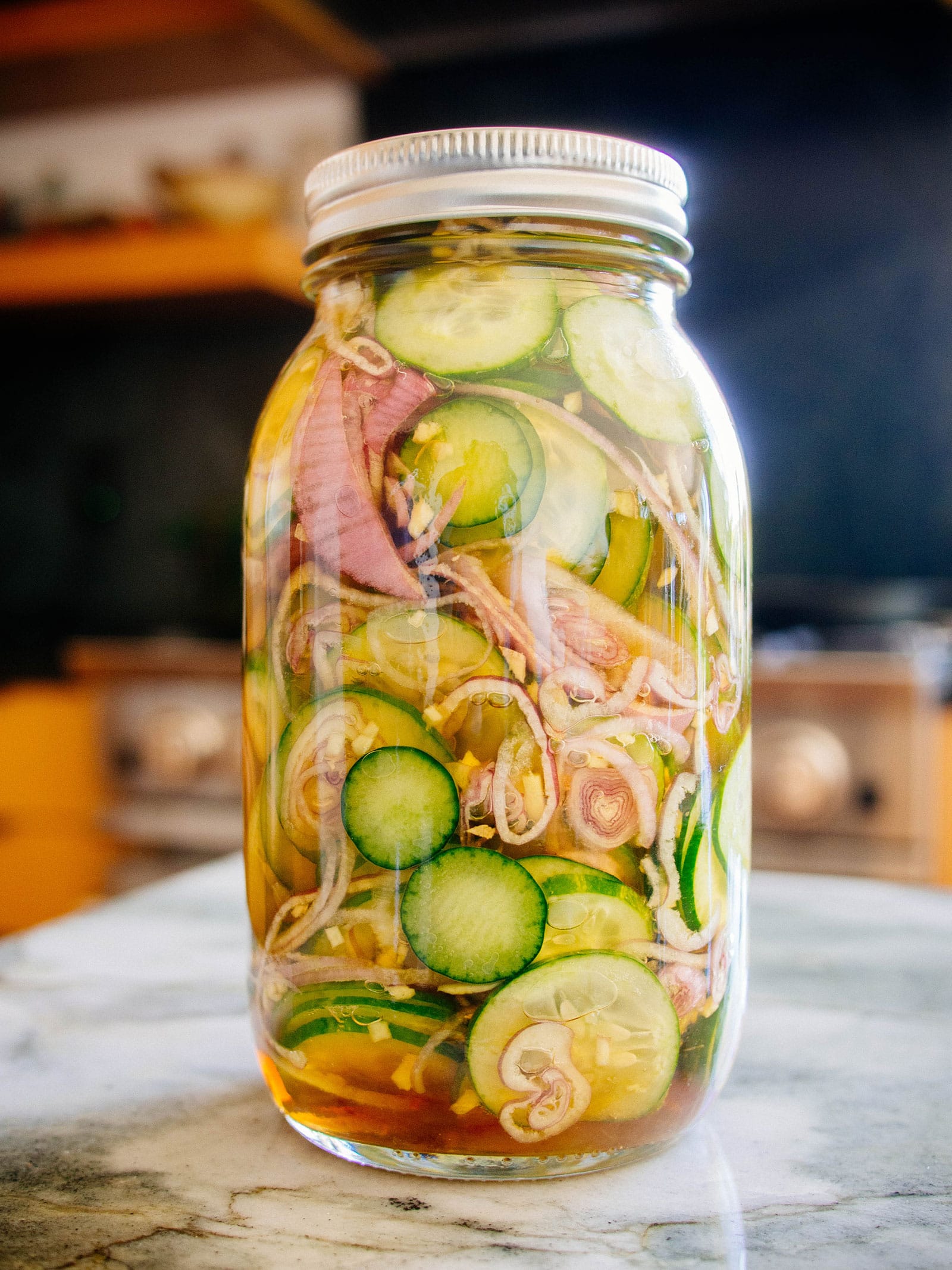 Jar of Asian quick pickled cucumbers and shallots sitting on a kitchen counter